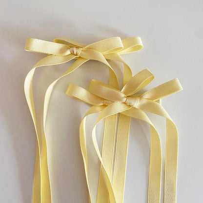 Light yellow bow ribbon hair clip displayed in a lifestyle scene, highlighting its soft fabric and elegant design in a natural setting.