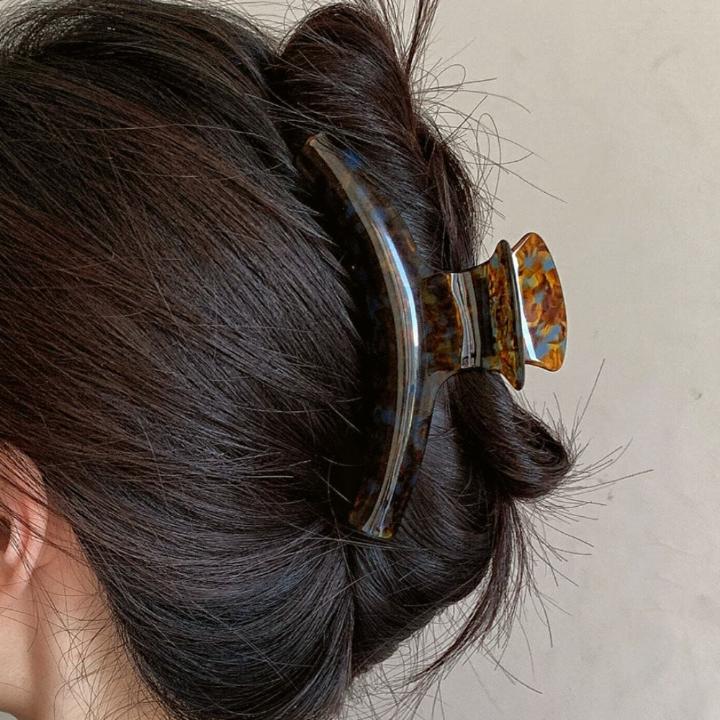 Lundi brown acetate claw clip displayed in a lifestyle scene, showcasing its glossy finish and sturdy design while elegantly holding hair in place.